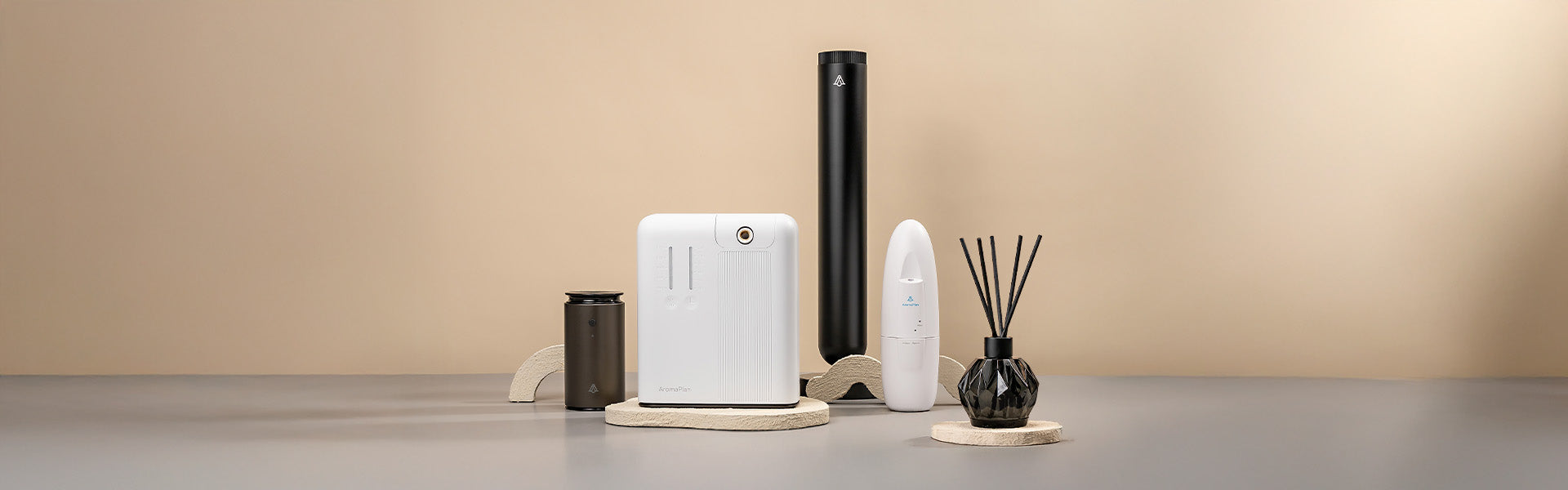 A set of four aroma diffusers with different shapes and sizes, displayed on beige stone-like stands. The background is a plain neutral beige color.