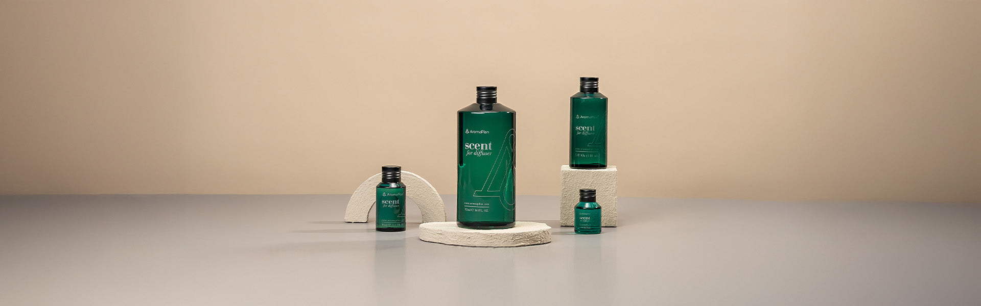  A collection of fragrance bottles labeled "Scent for Diffuser" in different sizes, with a green color theme, placed on beige stone-like pedestals on a simple gray surface.