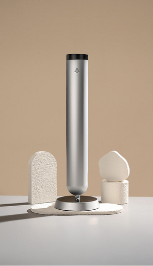 A slim, tall diffuser with a matte black finish, resting on a neutral background with simple geometric stone stands.